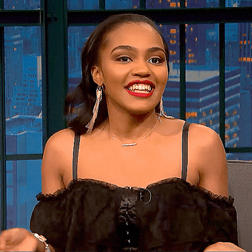 a woman wearing a black off the shoulder top and earrings is smiling