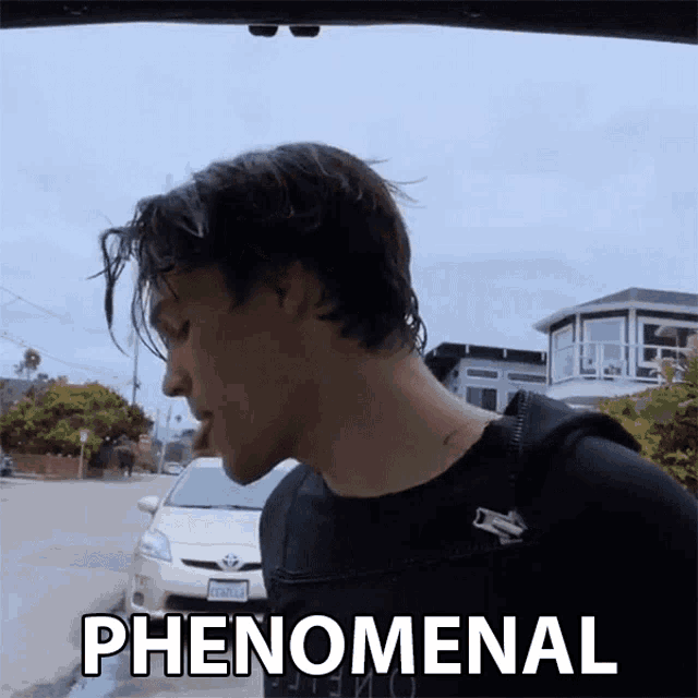 a man in a black shirt is standing in front of a car and the word phenomenal is on the bottom