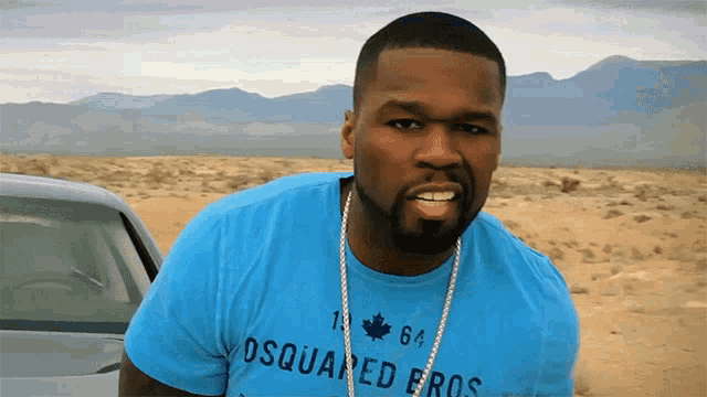 a man wearing a blue shirt that says dsquared eros stands in front of a car