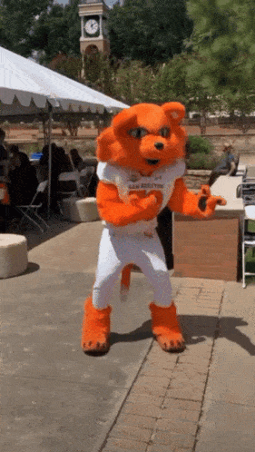 an orange and white mascot is dancing in front of a white tent