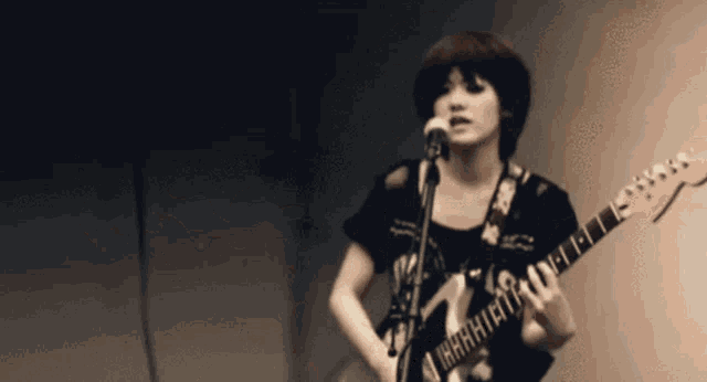 a woman is singing into a microphone while holding a guitar