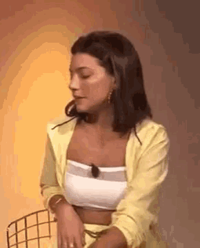 a woman is sitting in a chair wearing a yellow jacket and a white crop top .