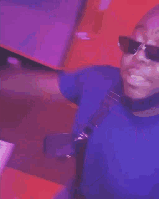 a man wearing sunglasses and a blue shirt is standing in front of a purple wall .