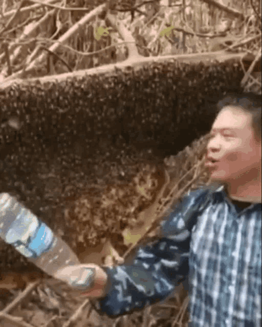 a man in a plaid shirt is holding a bottle of water in front of a beehive filled with bees .