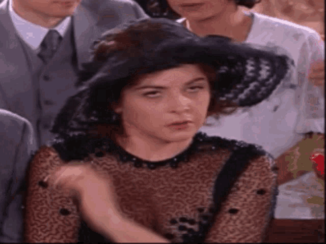 a woman wearing a black hat and a black dress is sitting in front of a group of people .