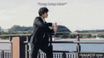 a man in a suit is standing on a bridge overlooking a body of water with the words long long man above him