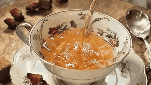 a cup of tea is being poured into a saucer next to a spoon .