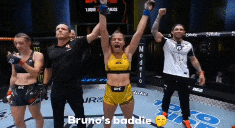 a woman in a yellow ufc top is holding up her arms in the air