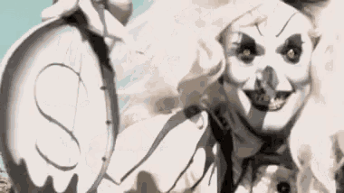 a scary clown is holding a clock in his hand and smiling .