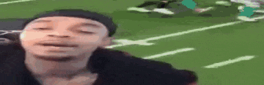 a man is standing on a football field with his eyes closed and making a funny face .