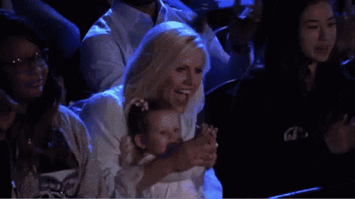 a woman is holding a baby with a pacifier in her mouth while sitting in a crowd .