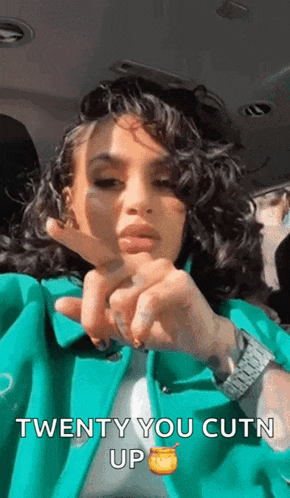 a woman in a green jacket is making a heart with her fingers and says twenty you cutn up .