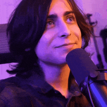 a man with long hair is sitting in front of a microphone .