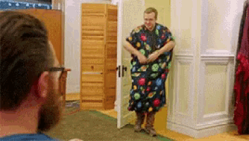 a man in a colorful robe is standing in a room with a bearded man looking at him .