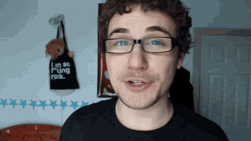 a man wearing glasses stands in front of a sign that says i 'm so f * cking rock