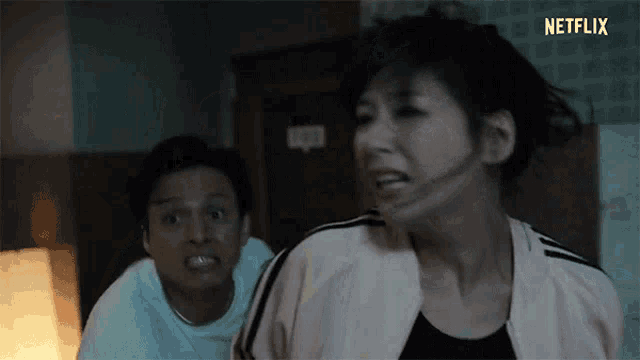 a man and a woman are standing next to each other in a room . the woman is making a funny face .