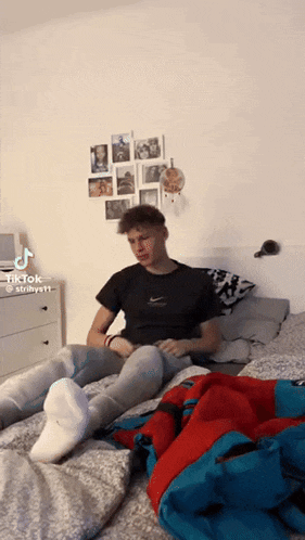 a young man is sitting on a bed wearing white socks and jeans .