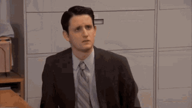 a man in a suit and tie is sitting at a desk and making a funny face .