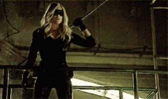 a woman in a black costume is standing on a railing holding a stick .