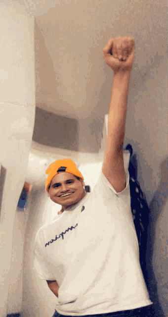 a man wearing an orange beanie and a white shirt that says " me " on it holds his fist up in the air