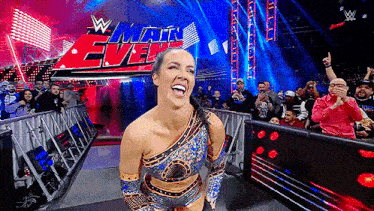 a female wrestler is standing in front of a crowd at a wrestling event and smiling .