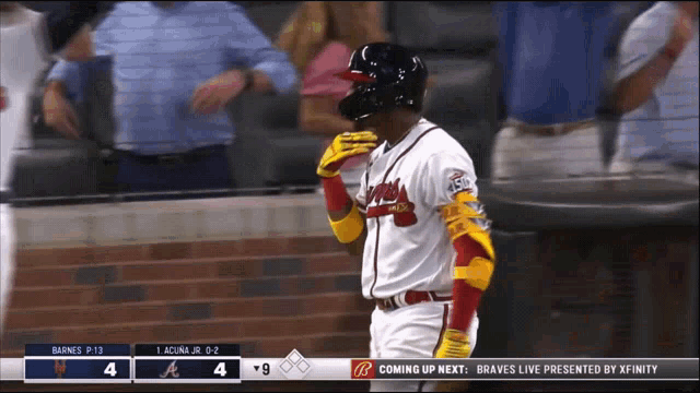 a baseball player wearing a helmet and gloves stands in front of a scoreboard that says " coming up next "