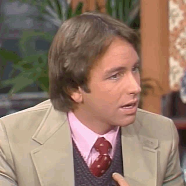 a man in a suit and tie is making a funny face while talking to someone .