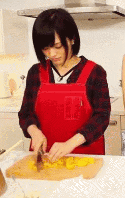 a woman in a red apron is cutting food on a wooden cutting board