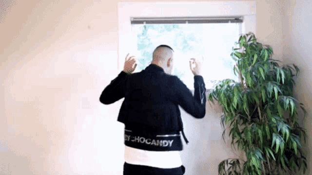 a man in a black jacket with the word chocandy on the back is looking out of a window .