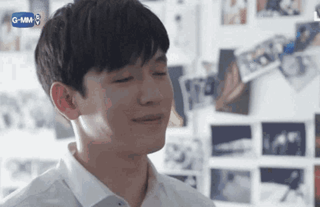 a young man in a white shirt is smiling with his eyes closed in front of a wall with pictures on it .