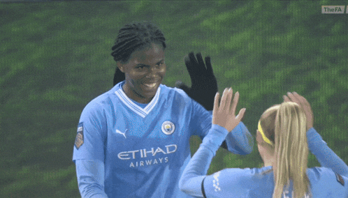 two female soccer players wearing etihad airways jerseys are giving each other a high five