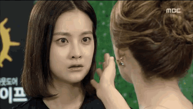 two women are looking at each other in front of a sign that says mbc on it