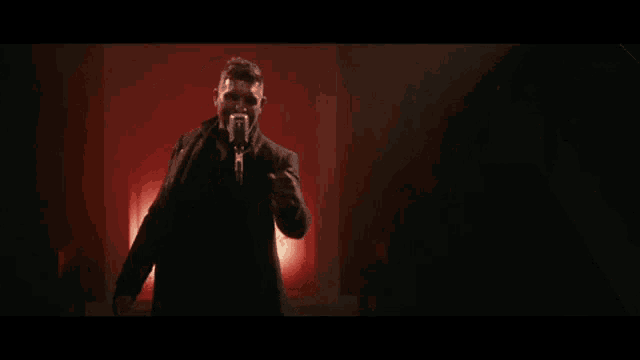 a man in a suit is standing in a dark room with a microphone in his hand .