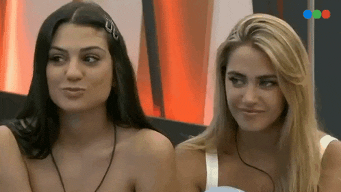 two women are sitting next to each other on a couch and looking at each other .