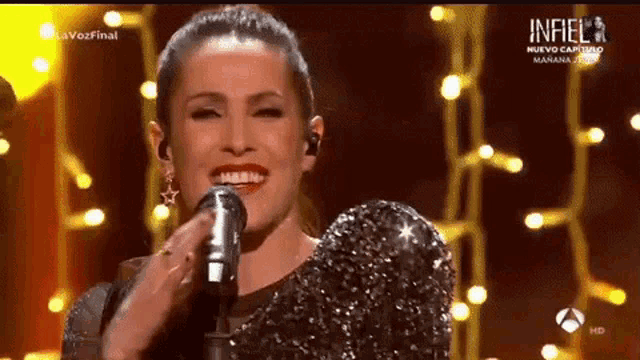a woman is singing into a microphone on a stage with lights in the background .