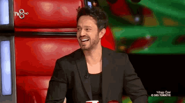 a man in a suit is sitting in a red chair and smiling .
