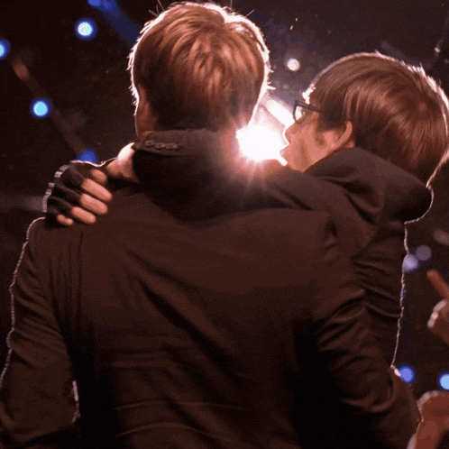 a man and woman are hugging in a dark room with the light shining on them