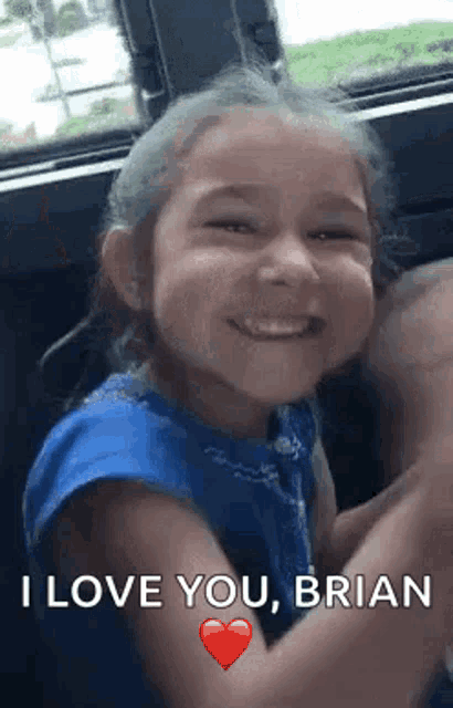 a little girl is sitting in the back seat of a car smiling and waving her hands .