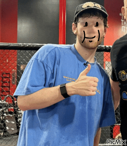 a man in a blue shirt with a smiley face drawn on his face is giving a thumbs up