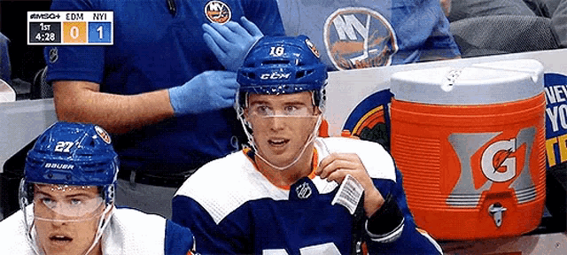 a hockey player wearing a blue helmet is sitting in the stands with a gatorade cooler in front of him .