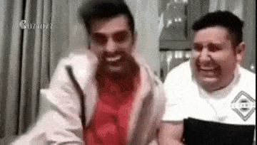 two men are laughing together in a room .