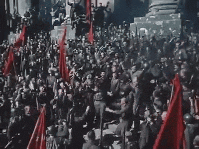 a large group of people holding red flags are standing in front of a building .