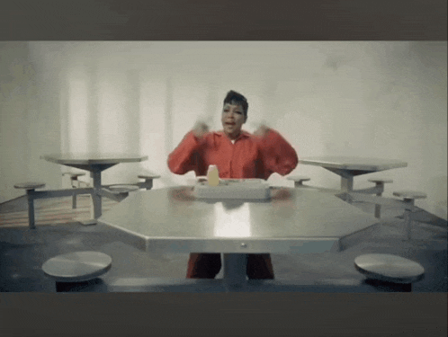 a woman in a red jumpsuit sits at a table with a tray of food on it