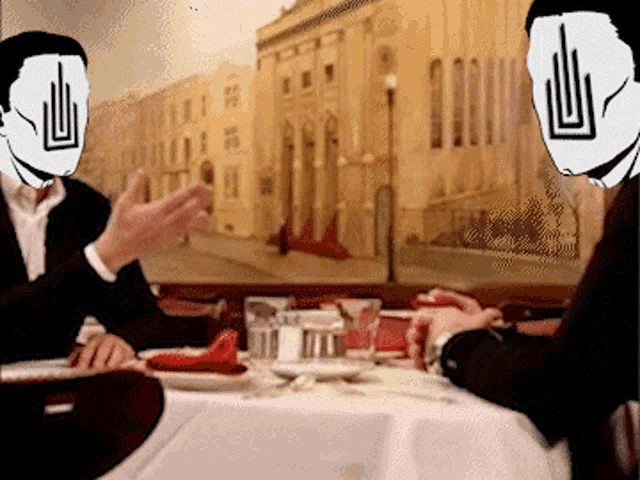 two men sitting at a table with masks on their faces and a building behind them