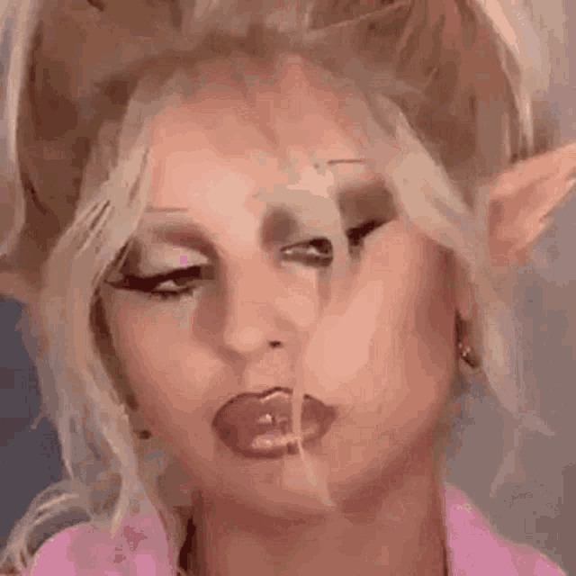 a woman with blonde hair and elf ears is wearing a pink shirt and earrings .