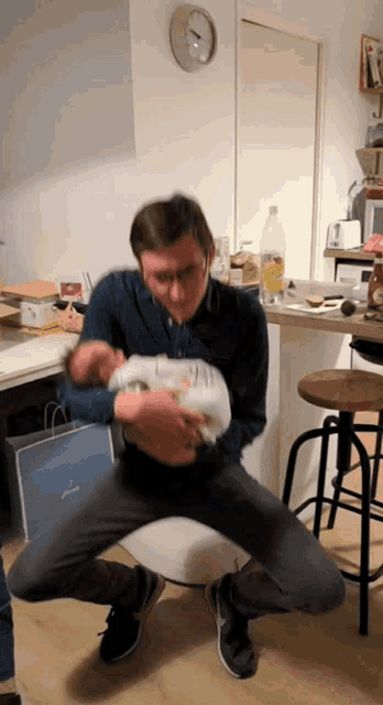 a man is holding a baby in his arms while sitting on a chair in a kitchen