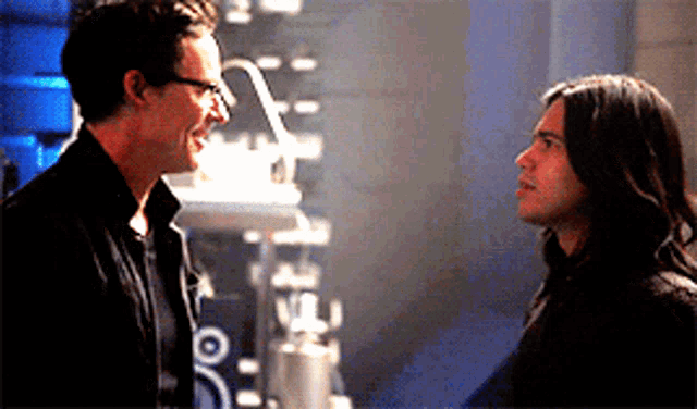 two men are standing next to each other in a dark room and looking at each other