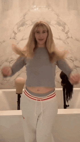 a woman in a crop top and white sweatpants is dancing in front of a mannequin .