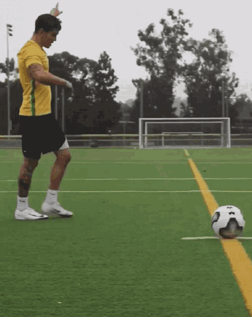a man in a yellow shirt and black shorts kicks a soccer ball on a field