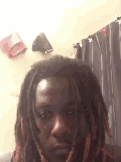 a man with dreadlocks is taking a selfie in front of a curtain .
